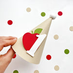 Handholding a mini kraft party hat with number 1 and red apple motif
