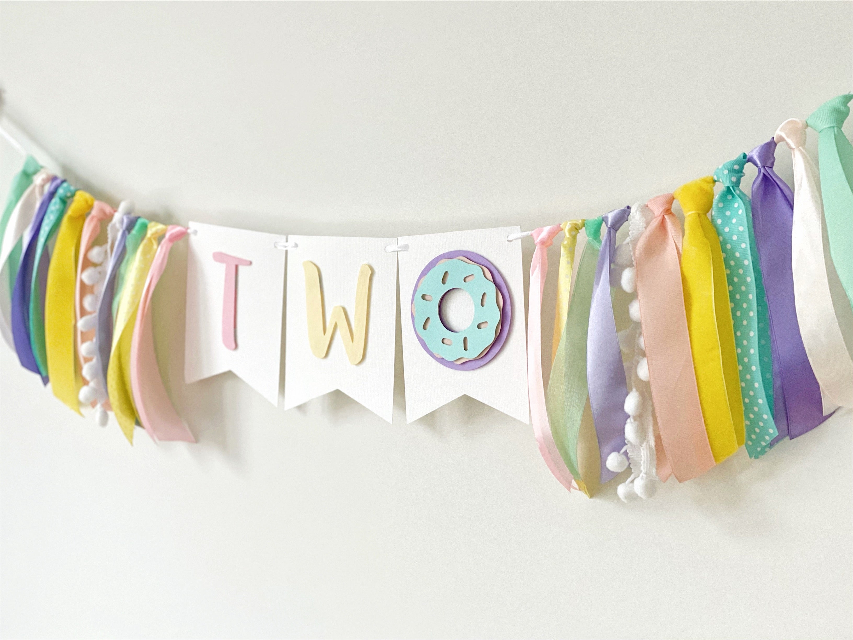 A pastel birthday banner spelling 'TWO' with a donut decoration