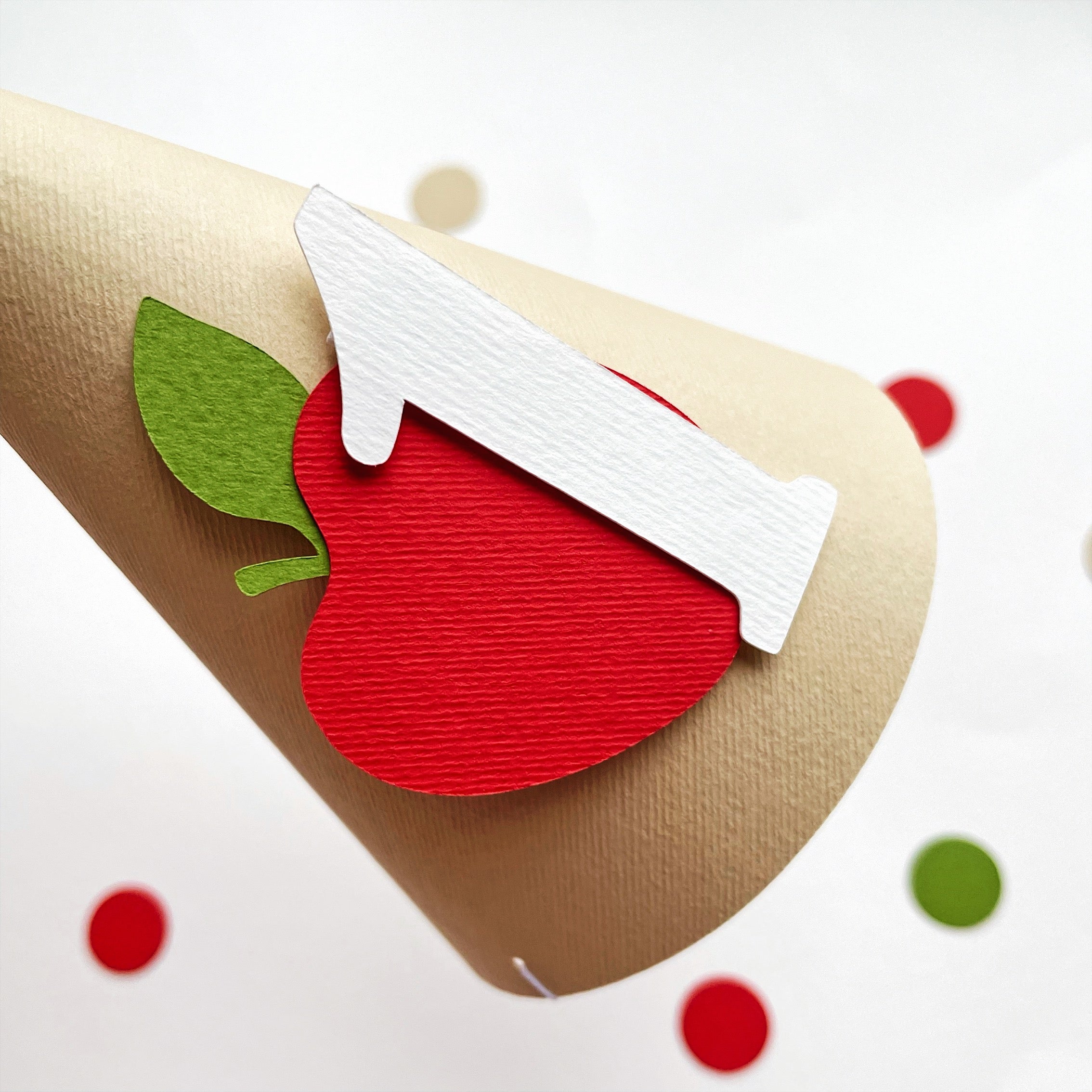Side view of 1st birthday apple party hat showing layered cardstock and pom pom