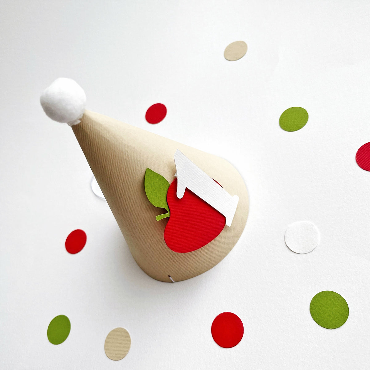 Apple theme 1st birthday cone hat surrounded by red and green table confetti