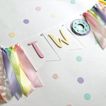 pastel birthday party decoration set featuring a 'TWO' banner with ribbon tassels, a donut decoration, and scattered pastel confetti 