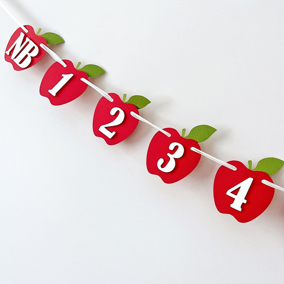 Full view of the red apple monthly photo banner pre-strung on twine for an orchard theme first birthday.
