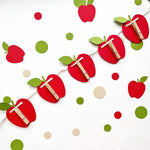Diagonal flat lay shot of handcrafted red apple cards with green leaves for monthly baby photos.