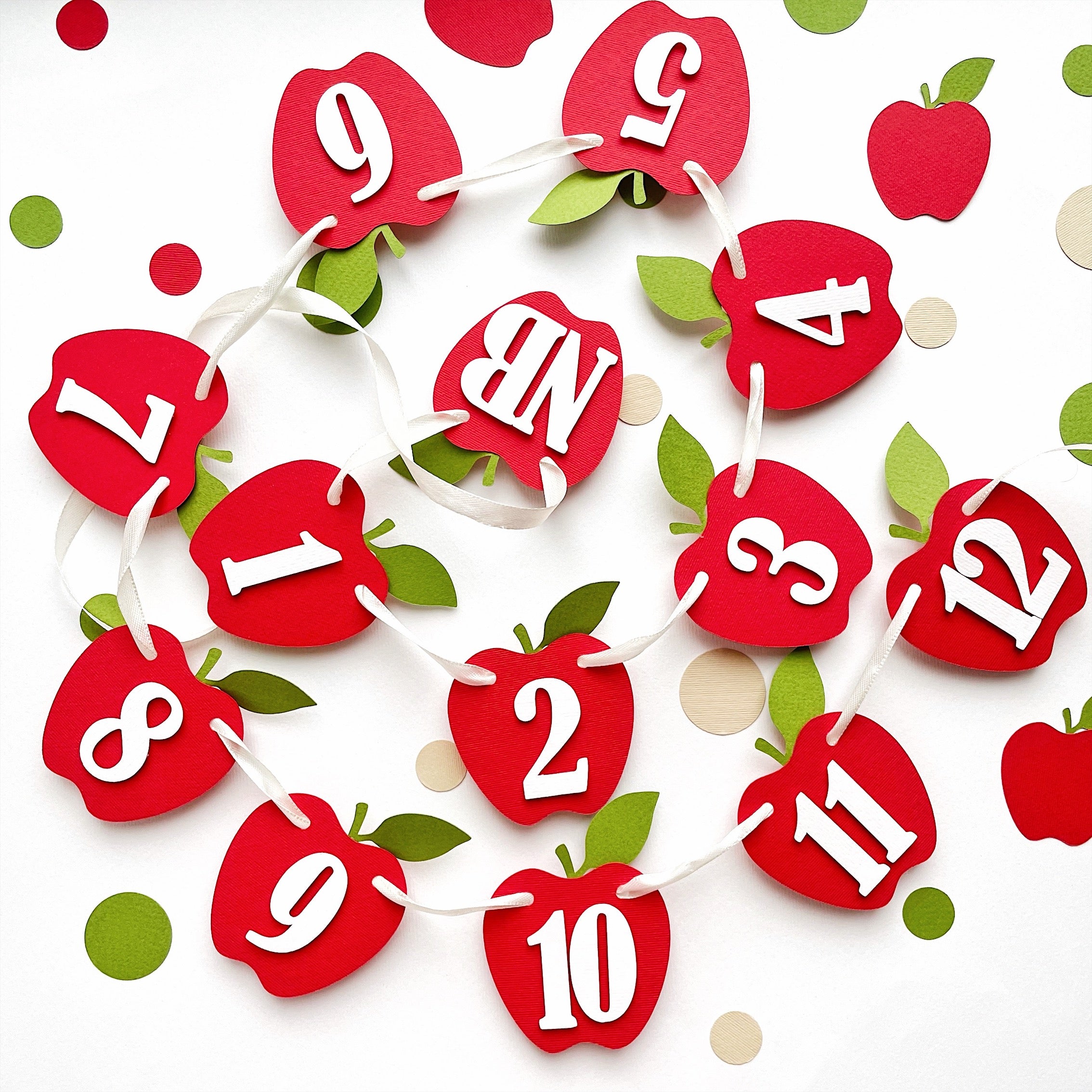 Scattered layout of red apple month cards from Newborn to 12 months for an Apple 1st Birthday theme.