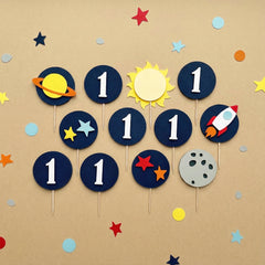 Space-themed 1st birthday cupcake toppers featuring a rocket ship, celestial stars, and solar system designs for a boy's first trip around the sun party.