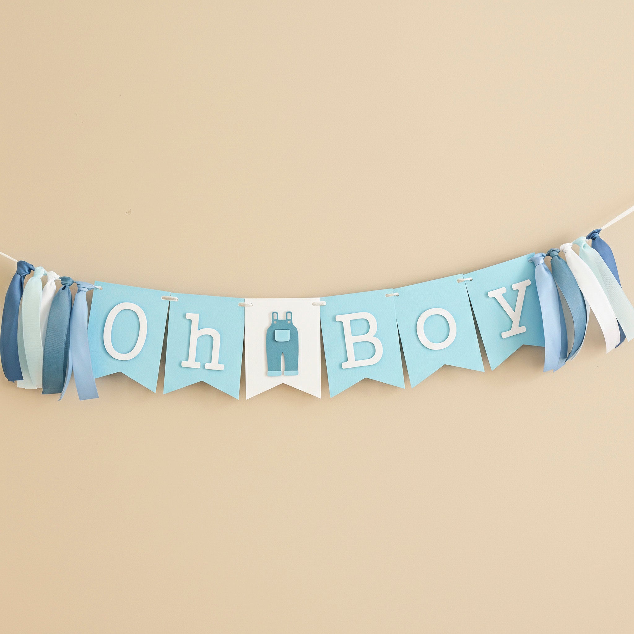 "Oh Boy" blue jean baby shower banner with light blue bunting flags, white letters, and a denim overall cutout, accented by blue and white ribbons.