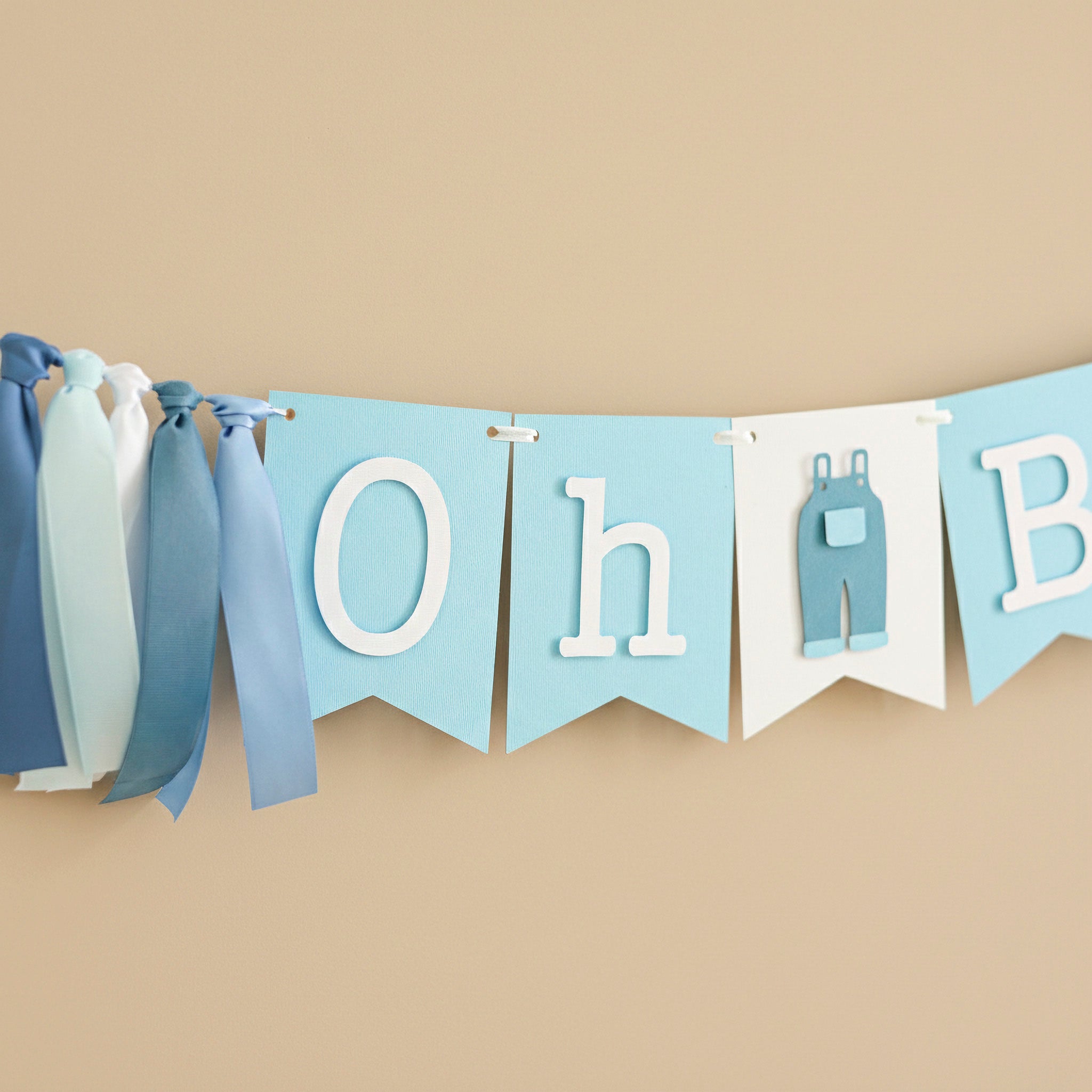 "Oh Boy" blue jean baby shower banner with light blue bunting flags, white letters, and a denim overall cutout, accented by blue and white ribbons.