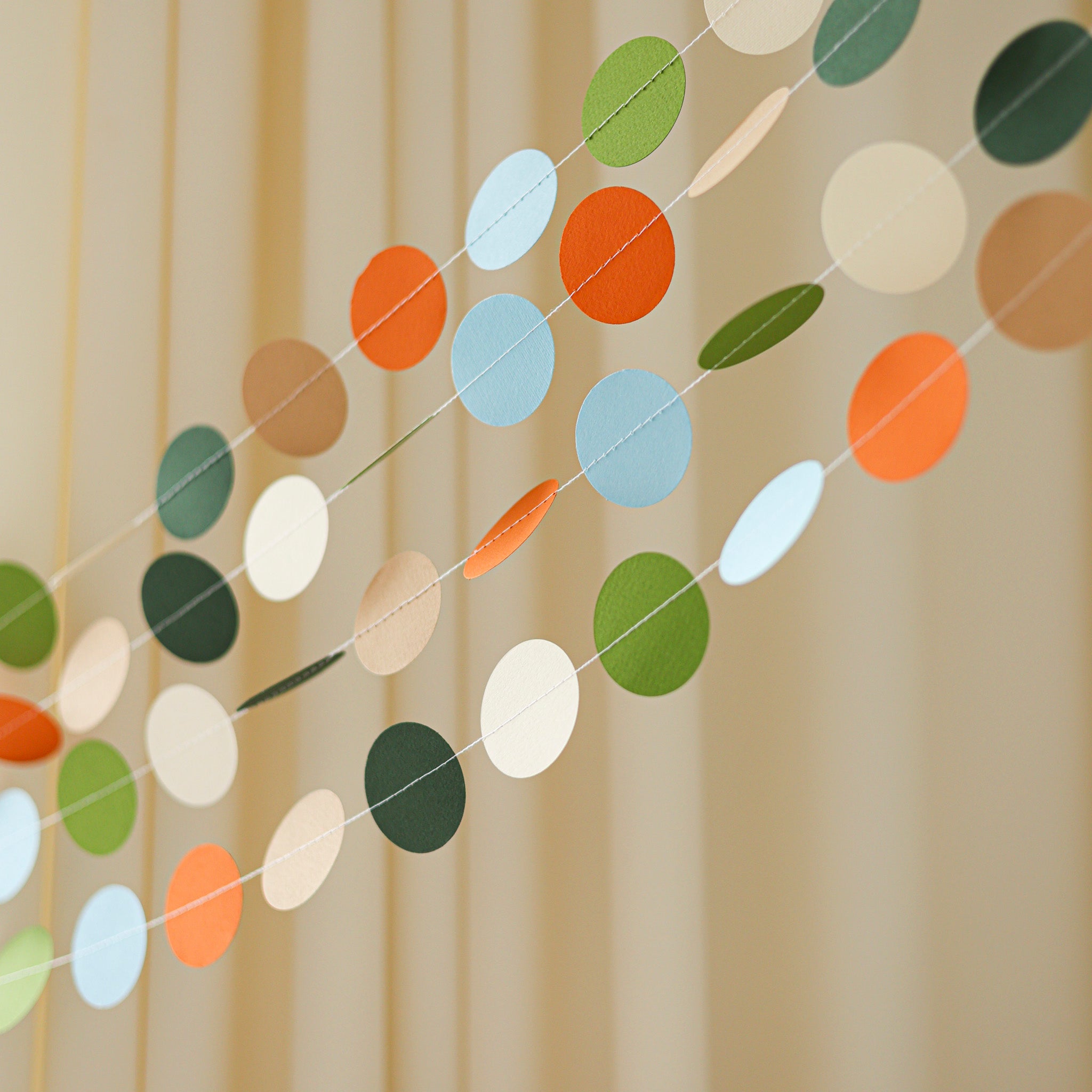 Multiple strands of earth-tone paper banners used as a wall backdrop for a Hatching Soon dinosaur-themed party.