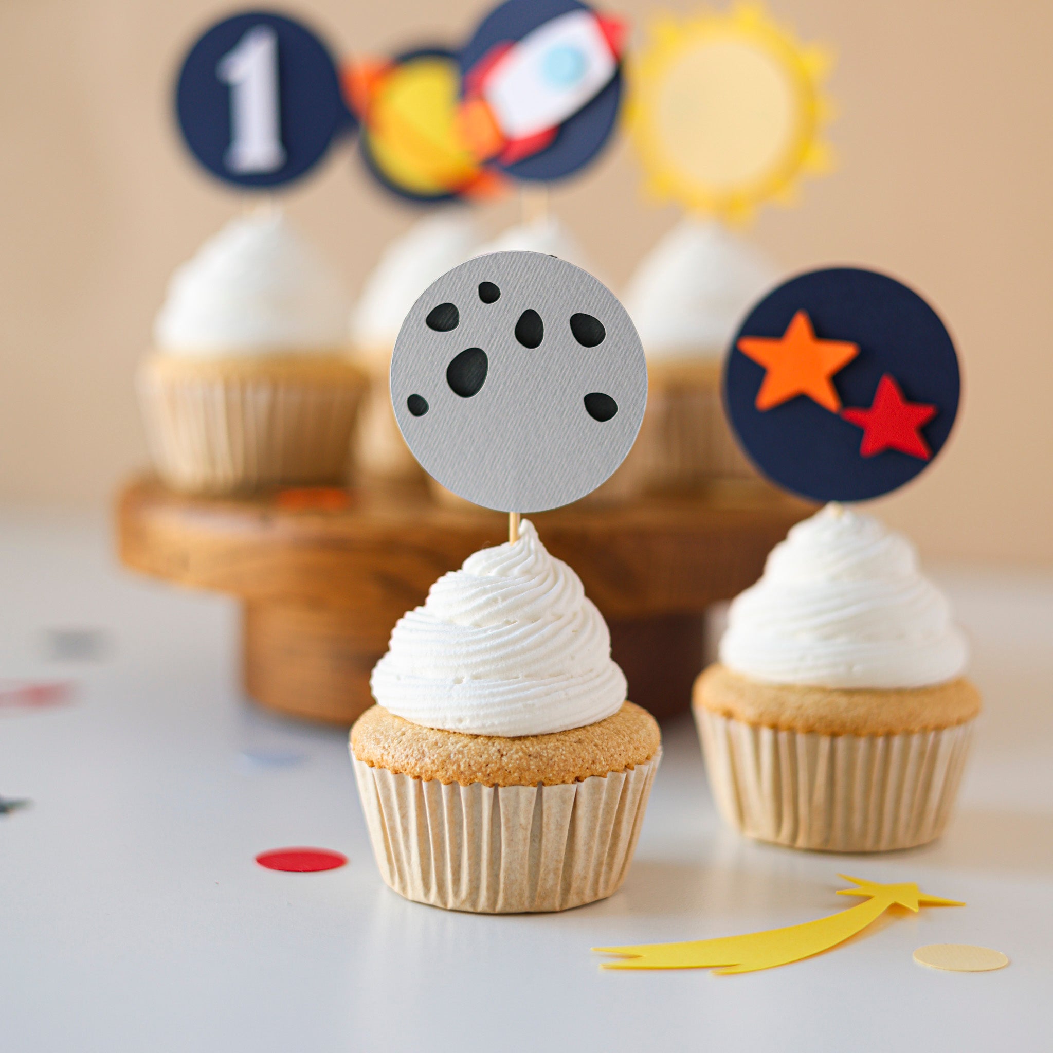 Close-up of layered cardstock space cake picks for a 1st birthday, showing a textured navy blue "1" topper and a detailed grey moon with craters.