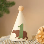 Side view of woodland birthday hat showing the soft elastic chin strap and fluffy tan yarn pom-pom.