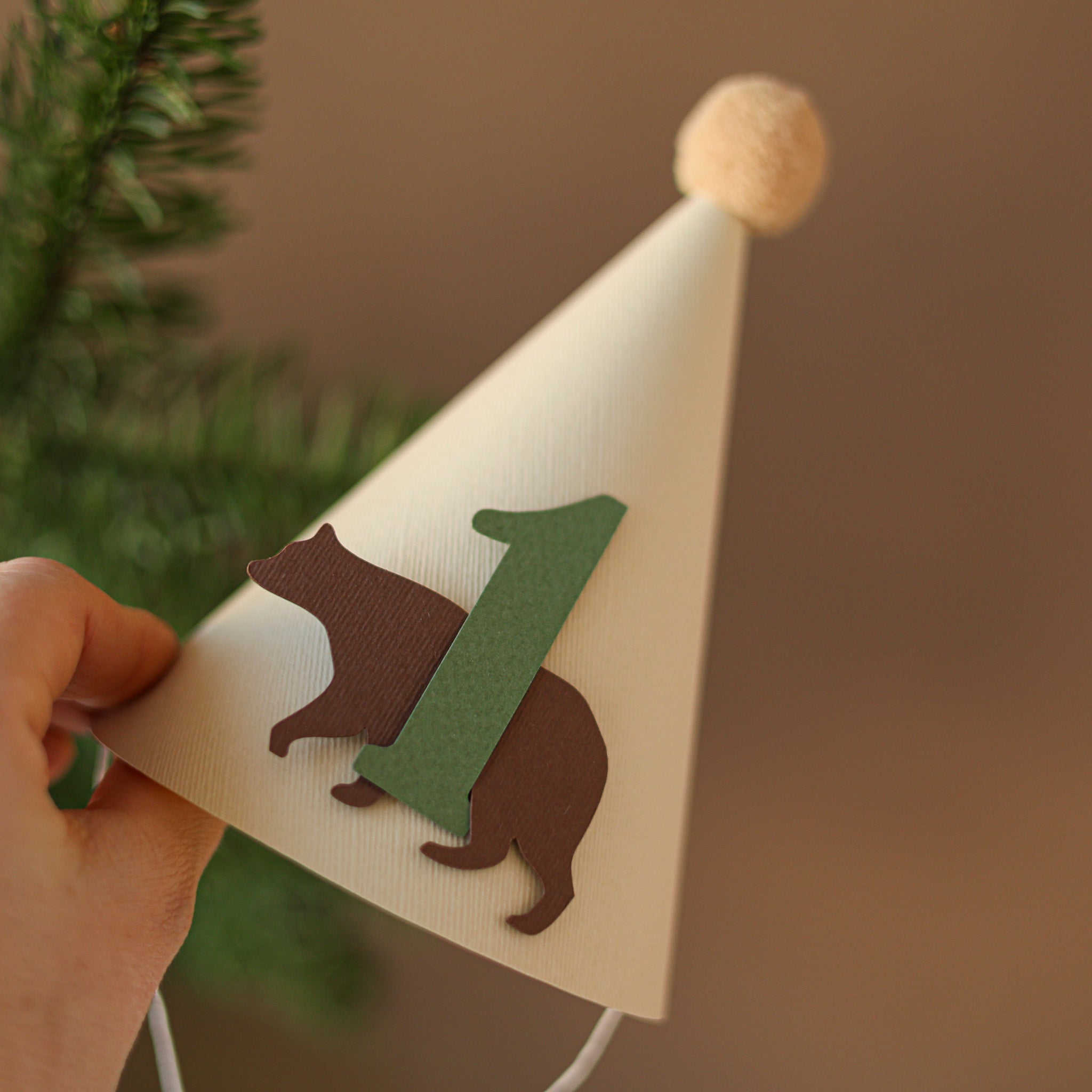 Handmade woodland bear first birthday party hat in cream with sage green number one and tan pom-pom.