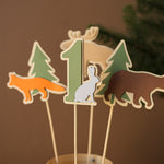 Close-up detail of paper moose, bear, and fox toppers in earth tones for an enchanted forest themed 1st birthday celebration.