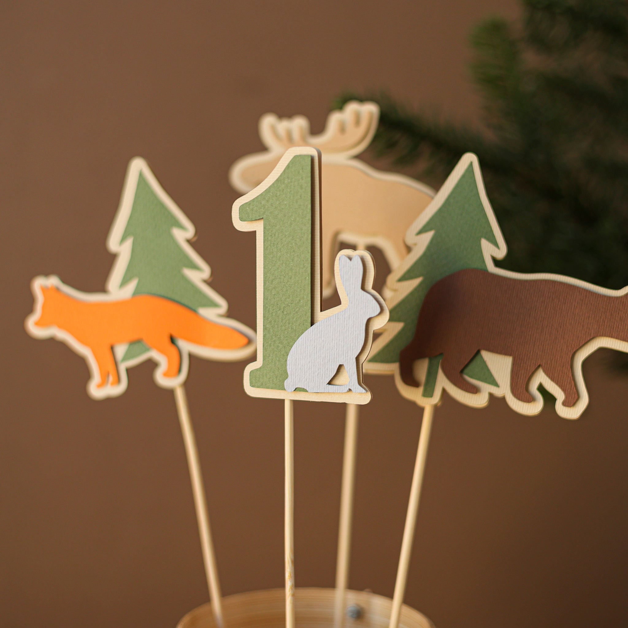 Close-up detail of paper moose, bear, and fox toppers in earth tones for an enchanted forest themed 1st birthday celebration.