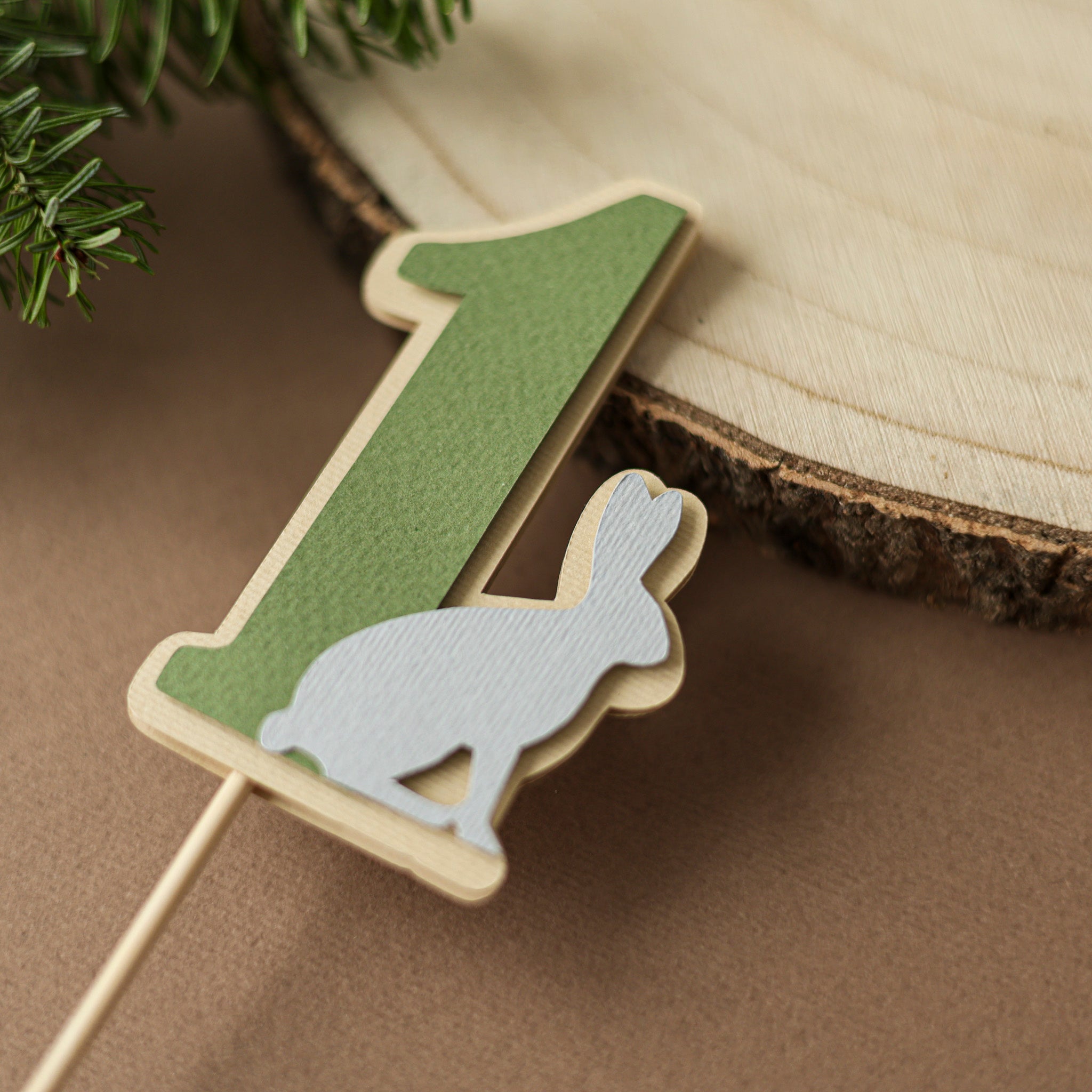 Sage green paper number one with a white rabbit cutout on a wooden dowel, woodland birthday table decor for a Wild One party.
