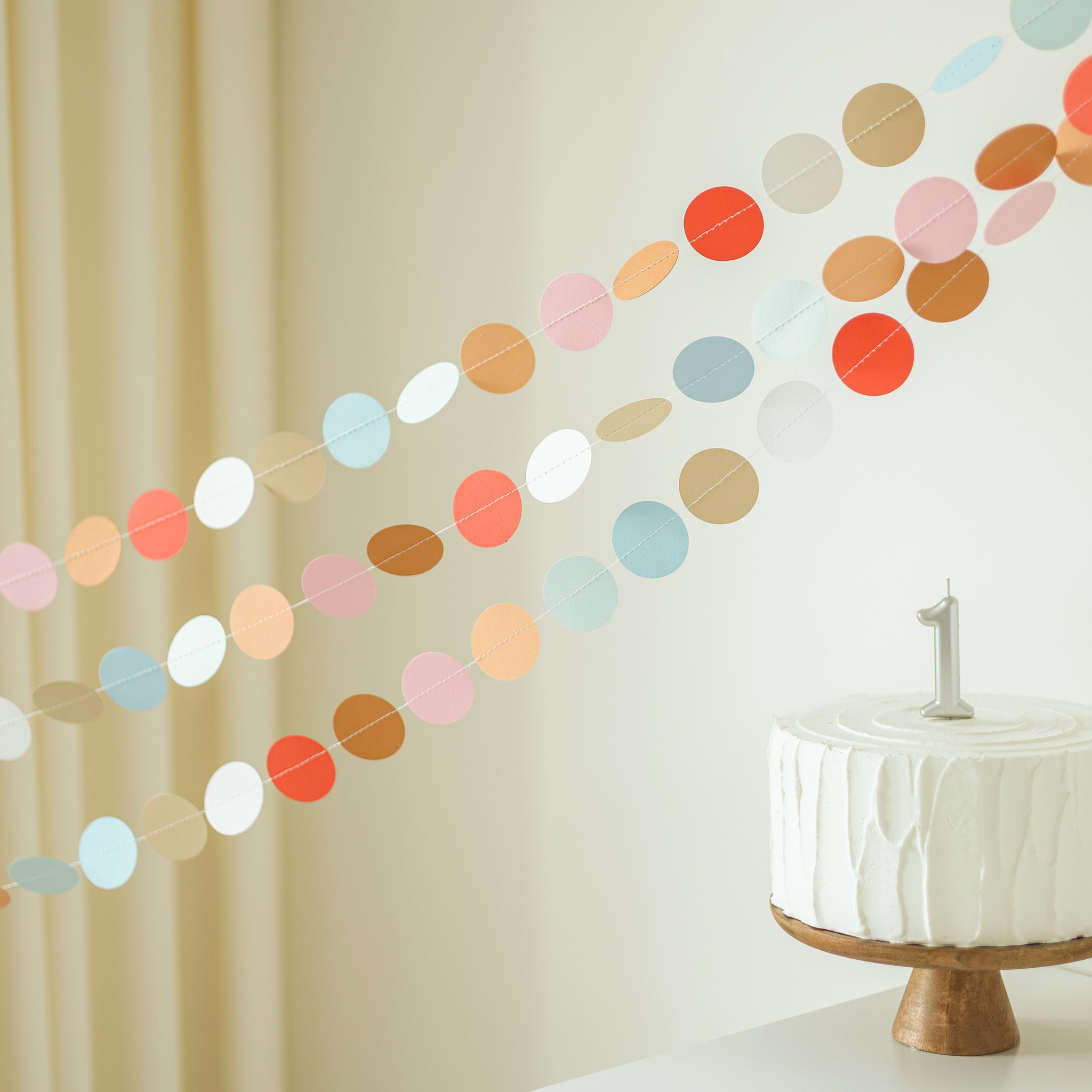 Colorful polka dot garland hanging on a wall with a white crib in the corner.