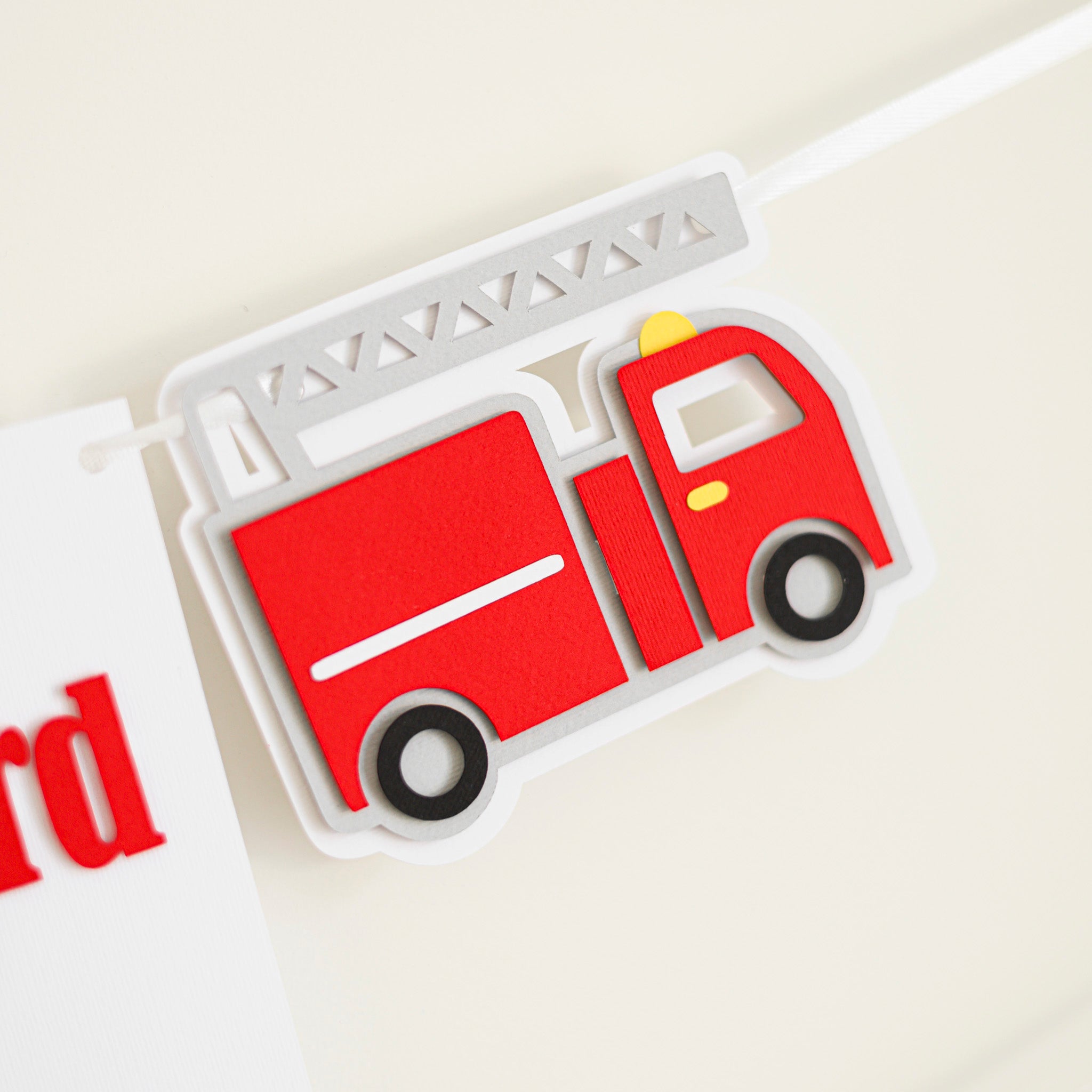 A white cardstock birthday banner with red lettering reading "HAPPY 3rd BIRTHDAY" flanked by red fire truck cutouts.