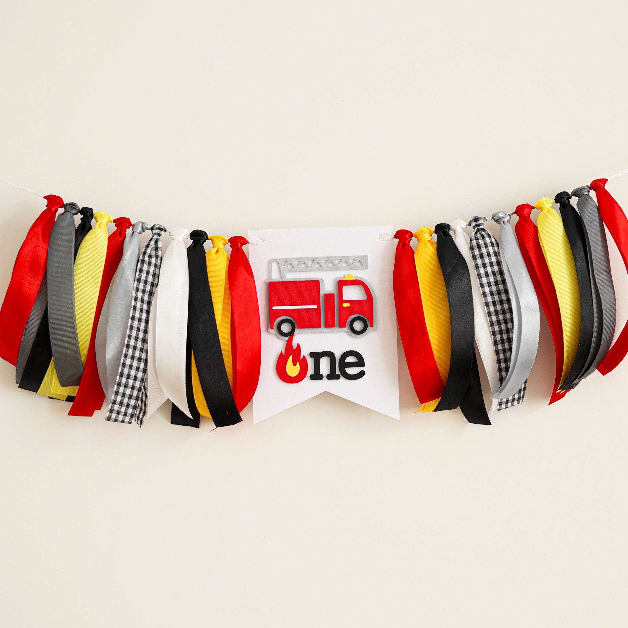 Firetruck 1st birthday highchair banner with red, yellow, and black ribbons featuring a 3D firefighter truck and "one" sign for a boy's cake smash.