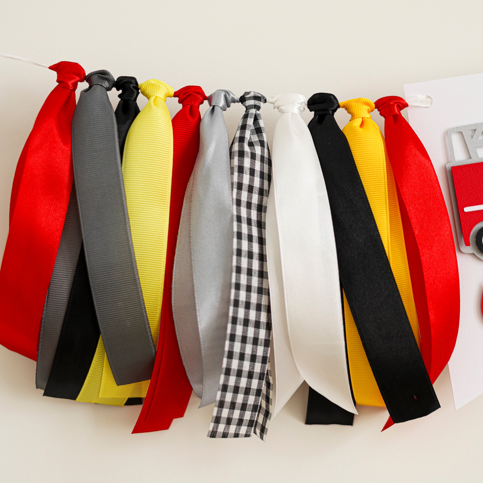 Full-length view of a fire truck ribbon garland for highchairs with adjustable white hanging cord and patterned gingham ribbons.