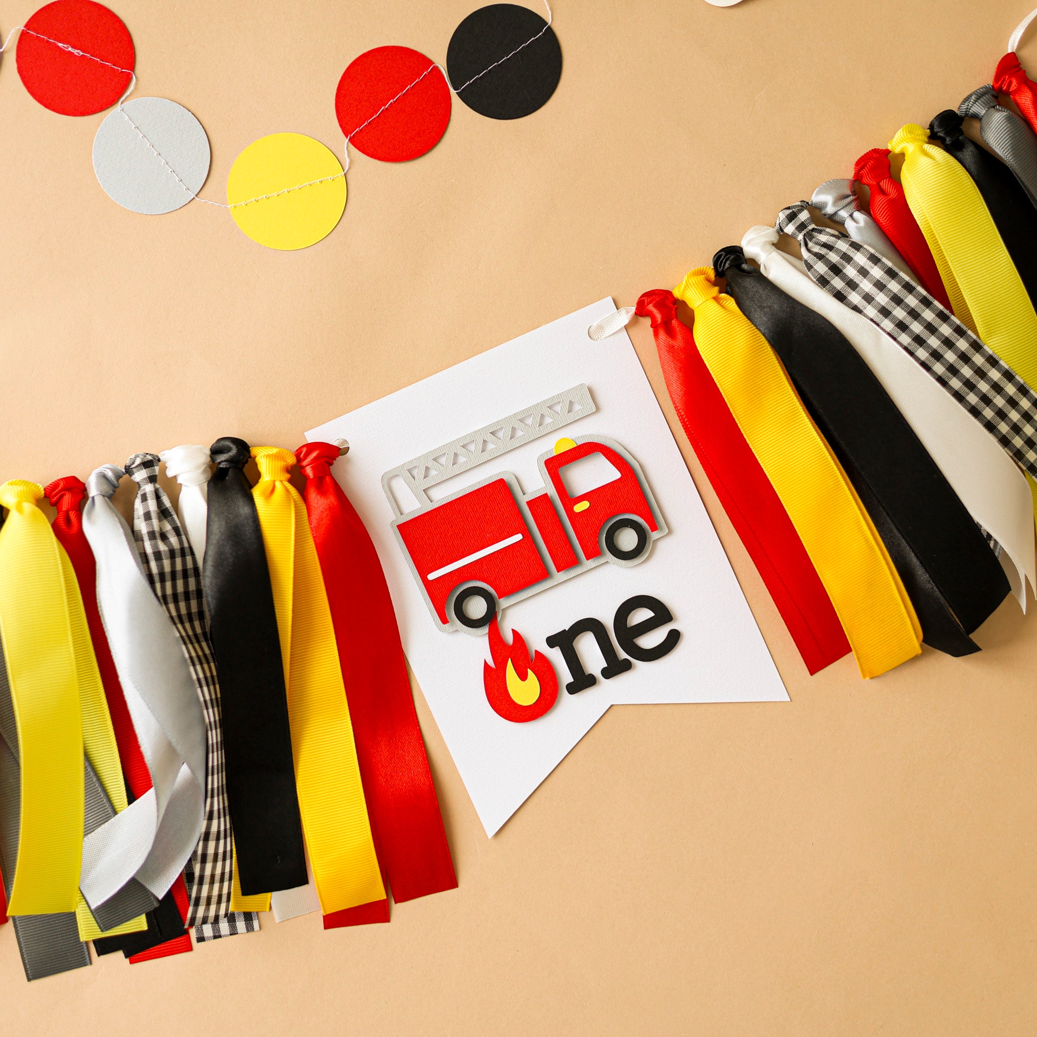 Firefighter themed first birthday party setup showing a ribbon garland highchair decoration and cake smash photo props.