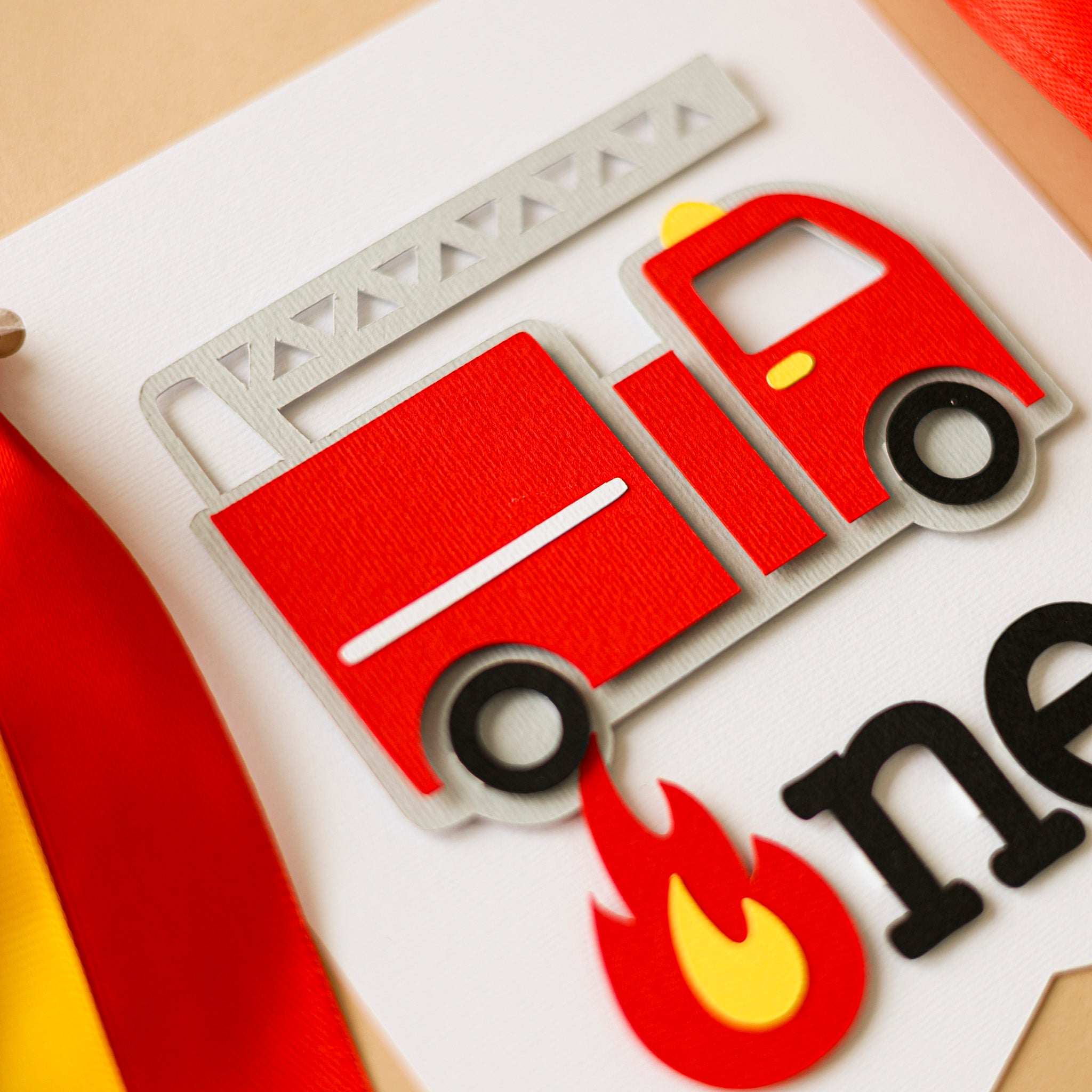 Detailed view of a handmade firefighter birthday pennant with a red fire engine and flame icon on white cardstock.