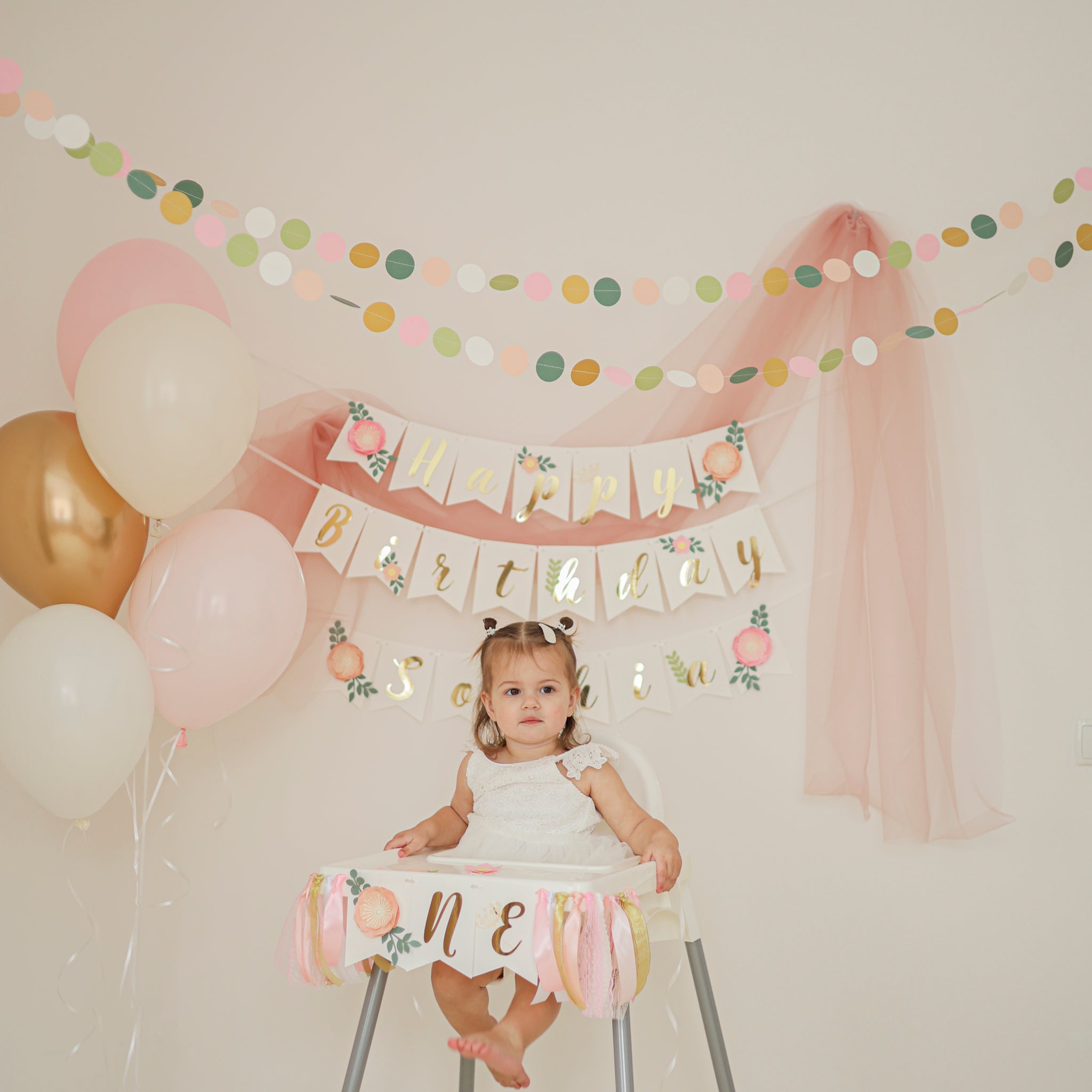Child in a high chair with 'Happy Birthday' banner and balloons, celebrating a special occasion.