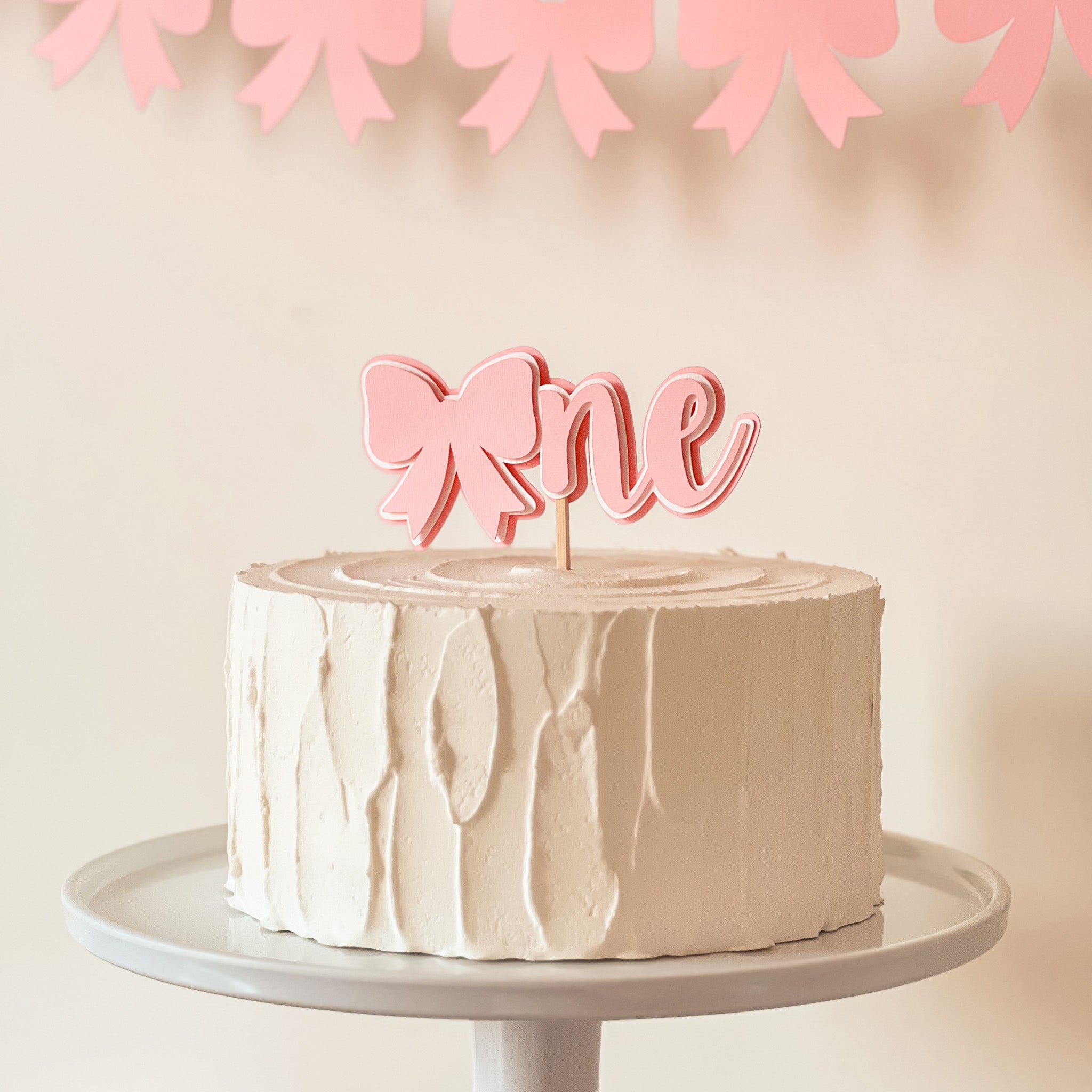 Pink bow cake topper on white frosted cake for coquette party decor