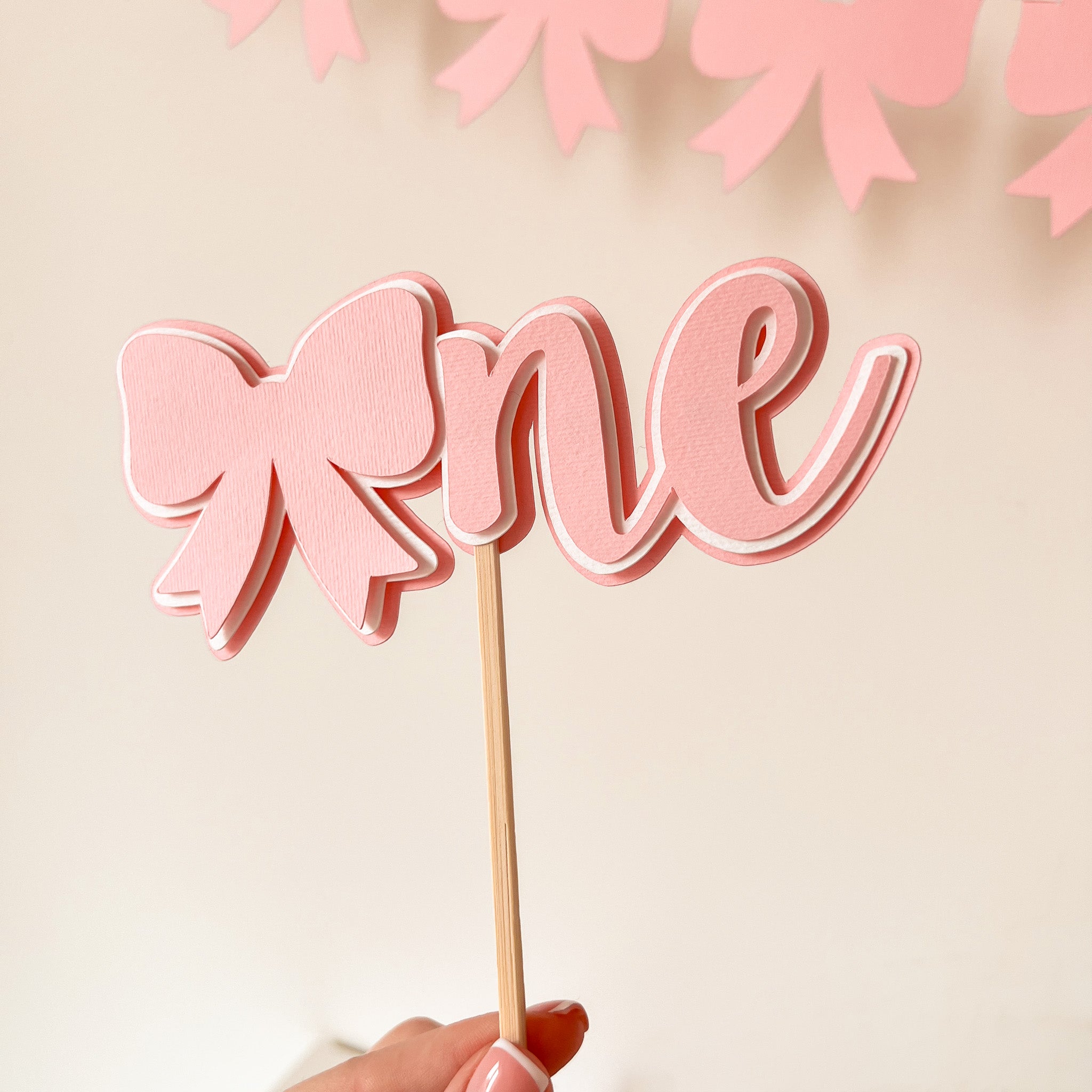 Detailed pink paper bow cake topper on wooden stick