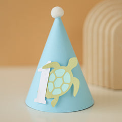 Light blue party hat with a turtle design and number '1' for baby boy ocean 1st birthday party