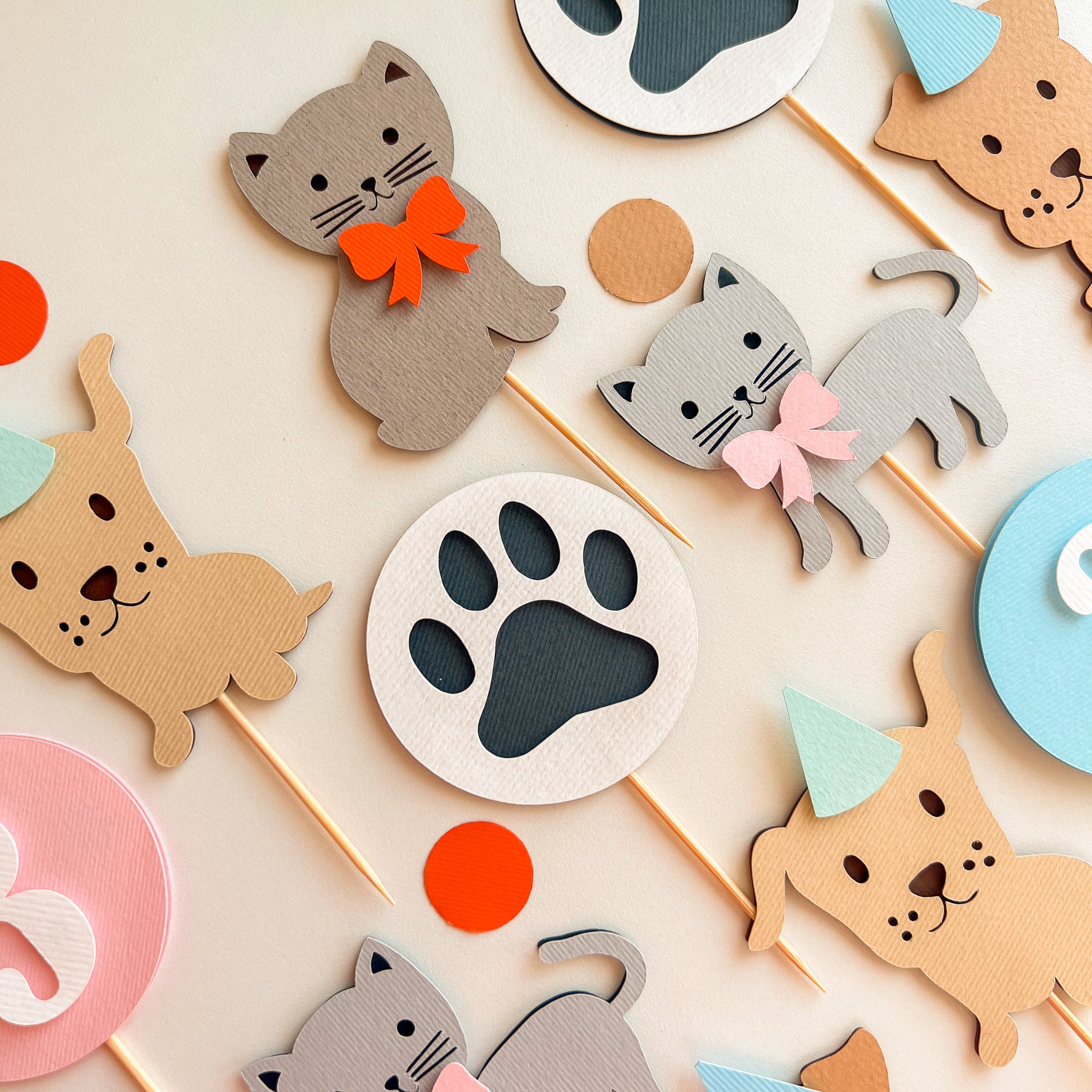 A styled Cat and dog party toppers on sticks, including gray and tan dog and cat figures with bows, paw print shapes, and pastel party hats