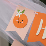 Close-up of a 'Little Cutie' themed first birthday banner. First birthday Little Cutie banner, orange citrus party decor, baby 1st birthday sign