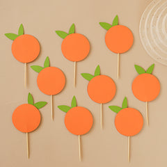 "Little Cutie" cupcake toppers, featuring bright orange circle cutouts with green leaves on wooden sticks, ideal for baby shower or 1st birthday party decorations