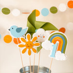 Colorful paper decorations including a bird, flower, cloud, rainbow, and number '1' in a metal bucket.