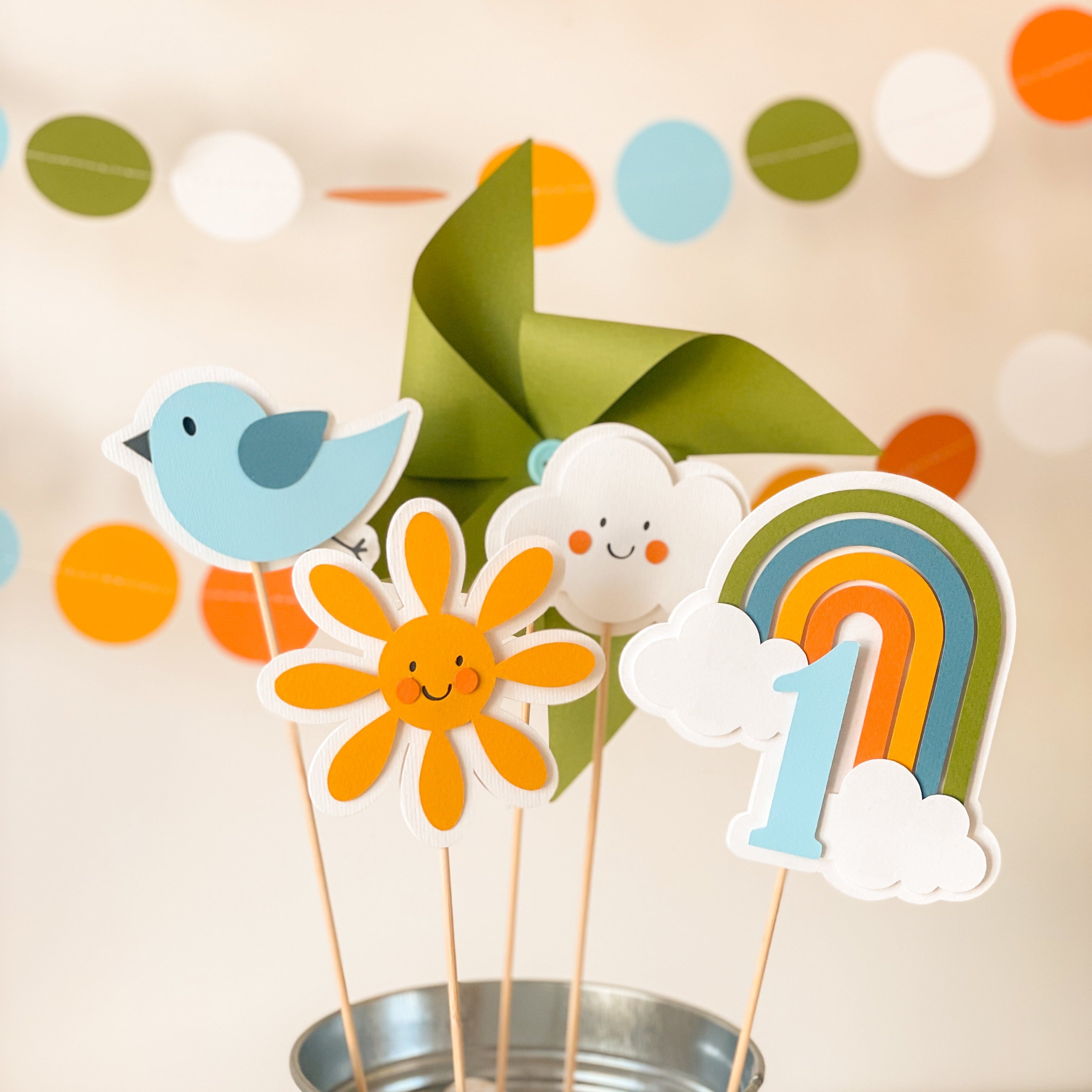 Colorful paper decorations including a bird, flower, cloud, rainbow, and number '1' in a metal bucket.