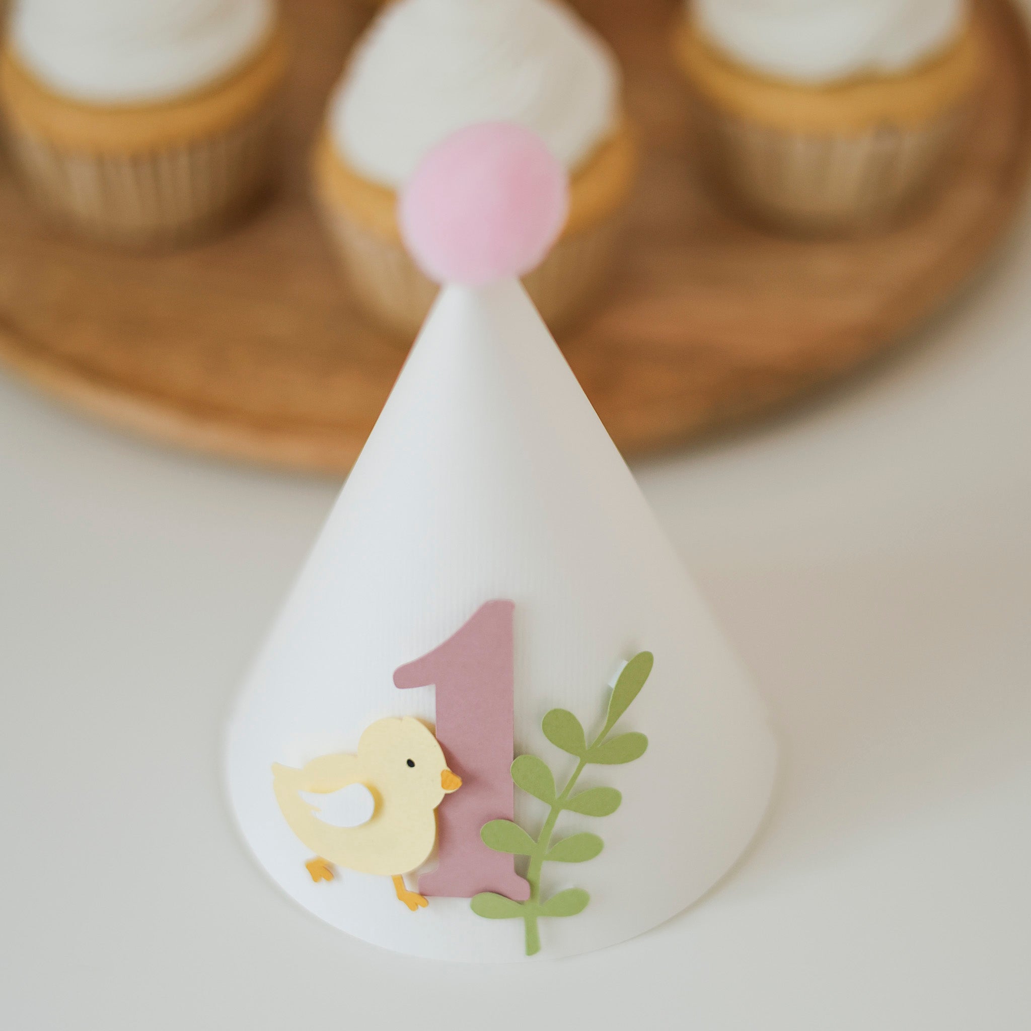 Handcrafted pastel yellow chick 1st birthday paper cone hat with dusty pink number one and light pink pom-pom