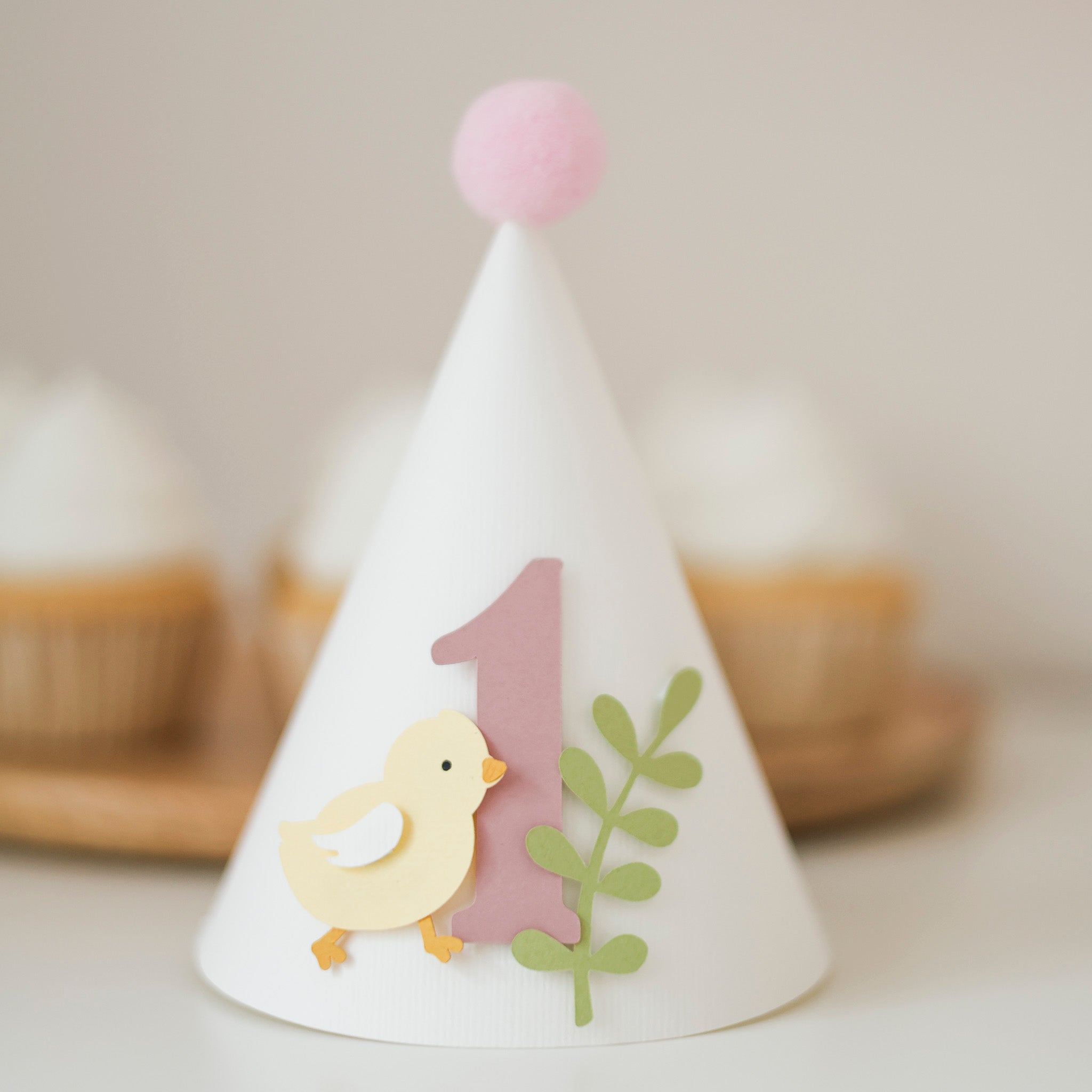 Handcrafted pastel yellow chick 1st birthday paper cone hat with dusty pink number one and light pink pom-pom