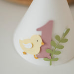 Handcrafted pastel yellow chick 1st birthday paper cone hat with dusty pink number one and light pink pom-pom