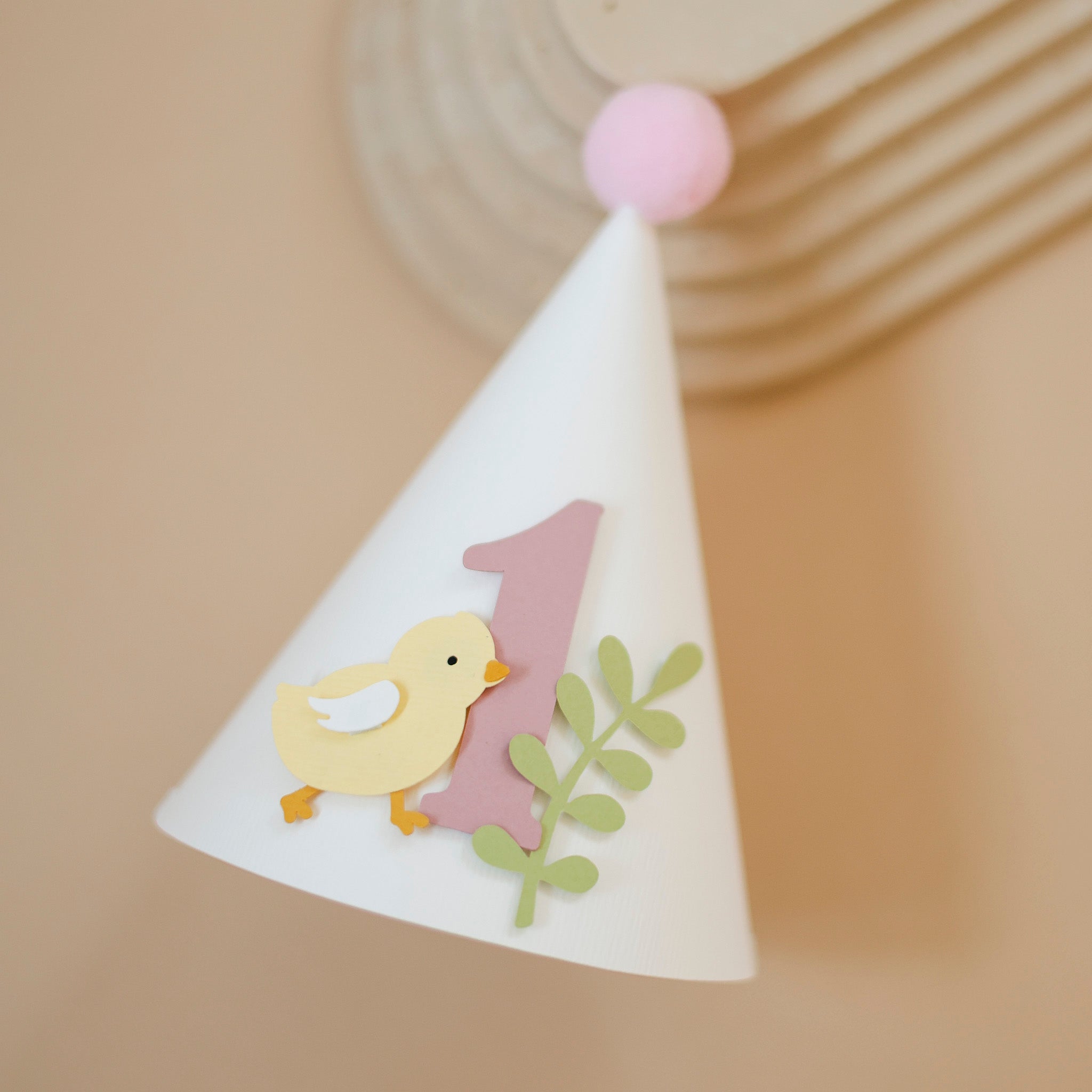 Handcrafted pastel yellow chick 1st birthday paper cone hat with dusty pink number one and light pink pom-pom