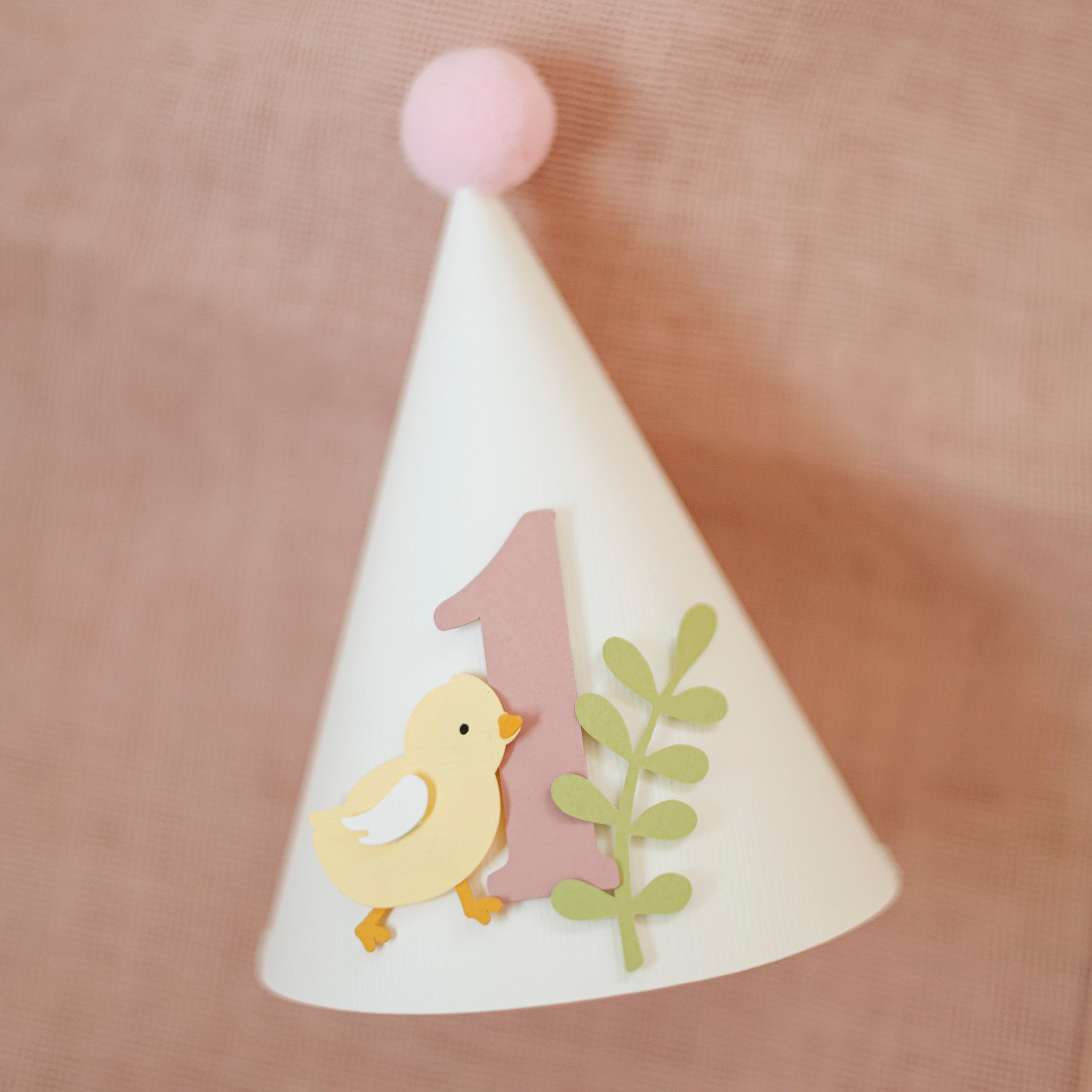 Handcrafted pastel yellow chick 1st birthday paper cone hat with dusty pink number one and light pink pom-pom