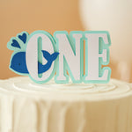 Cake topper with 'ONE' and whale design on a cake