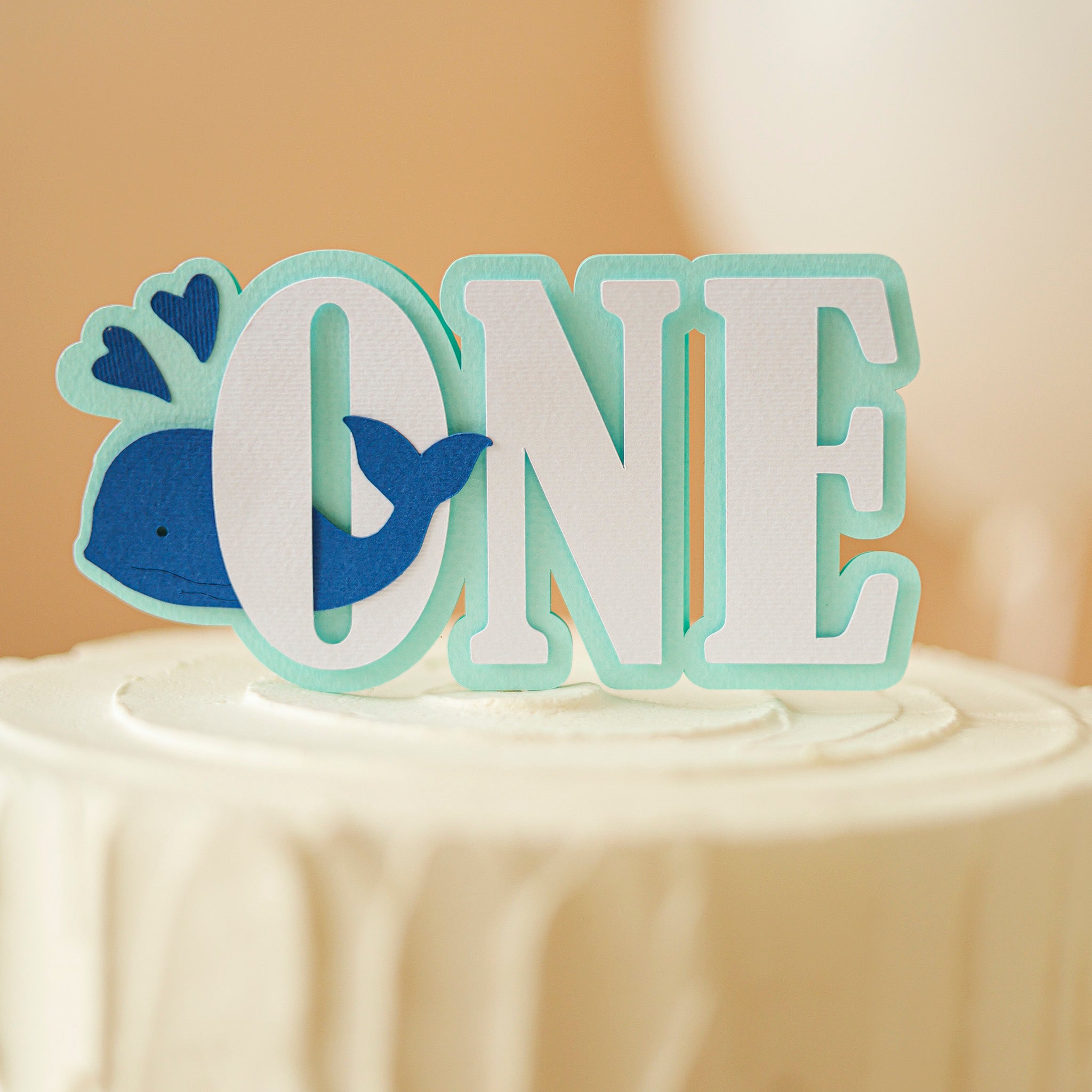 Cake topper with 'ONE' and whale design on a cake