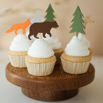 Woodland animal cupcake toppers for a forest baby shower or wild one birthday, featuring paper cutouts of bears, foxes, moose, and pine trees in earthy tones.