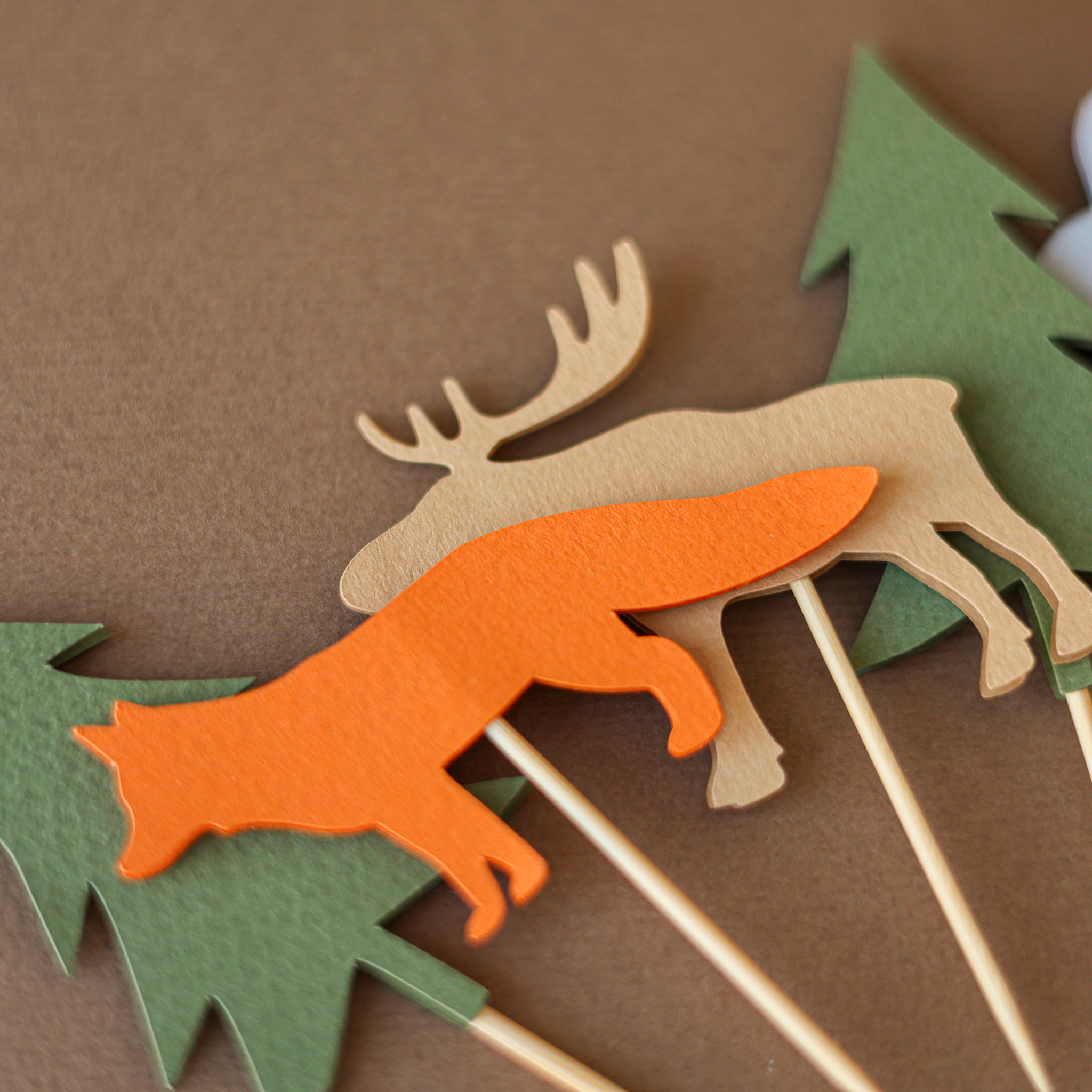 Woodland animal cupcake toppers for a forest baby shower or wild one birthday, featuring paper cutouts of bears, foxes, moose, and pine trees in earthy tones.